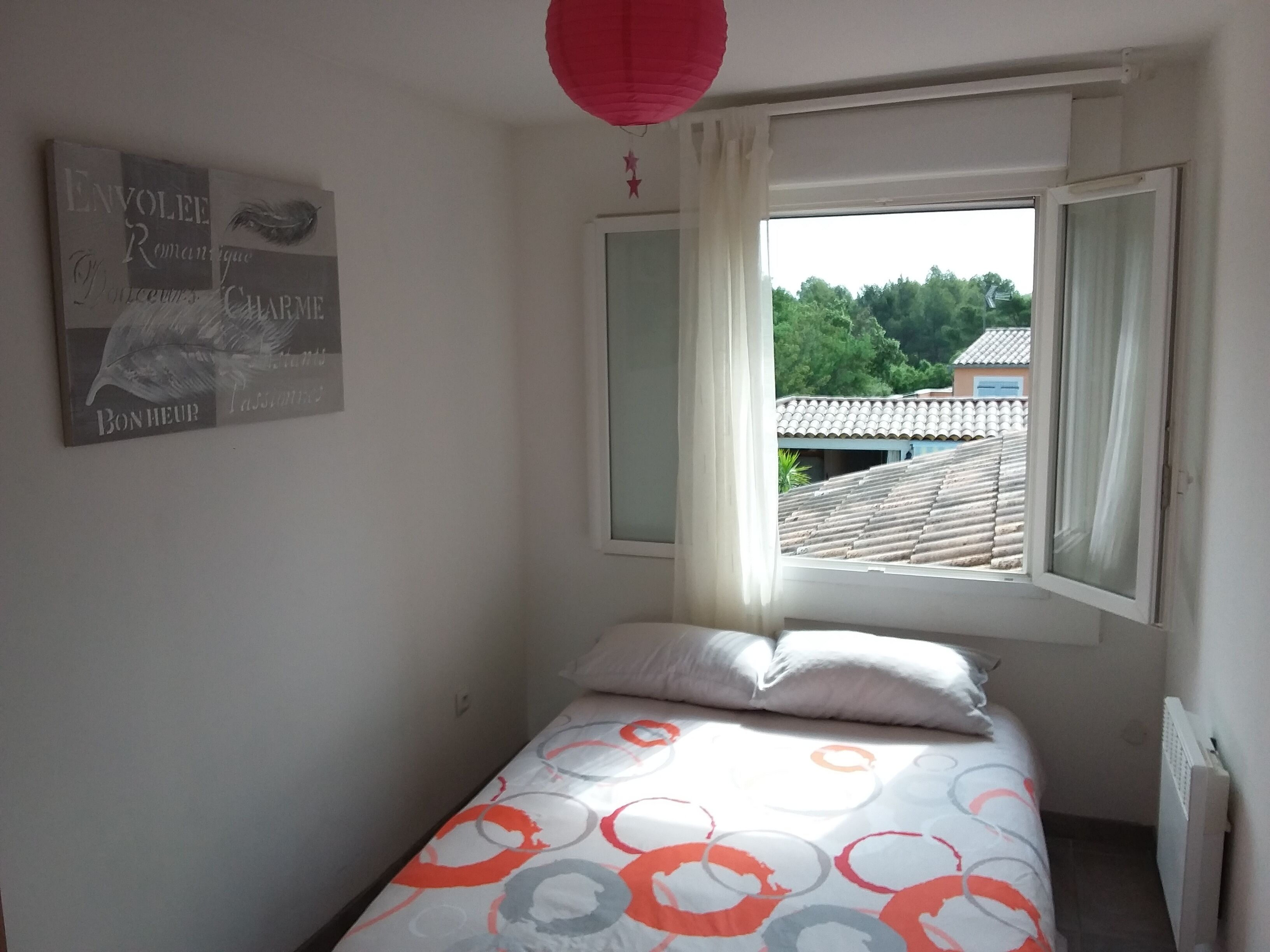 Une chambre à coucher avec un lit, une fenêtre avec des rideaux et un mur orné d’une affiche.