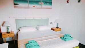 Een keurig opgemaakt bed met een wit hoofdbord, twee nachtkastjes met lampen, en een wandeling schilderij van een strandgezicht.
