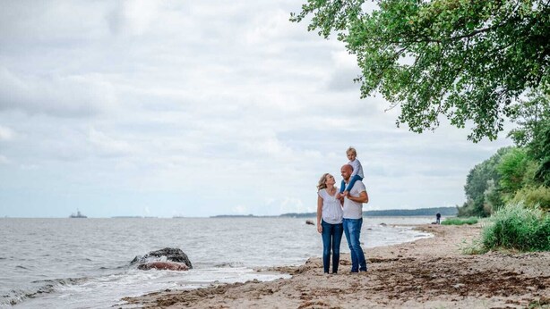 A beach scene with a family standing on the shore, a ship in the distance, and a cloudy sky. - Cozy tiny house on the Greifswalder Bodden (Brünzow)