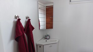 A bathroom with a white sink, a mirror, a toilet, and two red towels hanging on a metal towel rack. - Cozy tiny house on the Greifswalder Bodden (Brünzow)