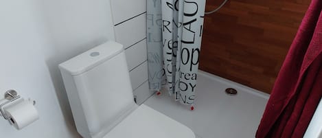 Un baño con inodoro blanco, ducha con cortina blanco y negro, y piso de madera.