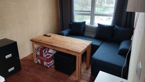 A small, cozy room with a wooden table, a blue sofa, a black filing cabinet, and a suitcase labeled "LONDON" on the floor. - Cozy tiny house on the Greifswalder Bodden (Brünzow)
