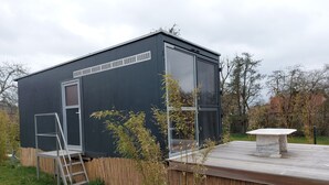 A modern, compact building with a large sliding glass door, a small outdoor seating area, and a wooden deck. - Cozy tiny house on the Greifswalder Bodden (Brünzow)