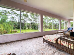 Una habitación con ventanas amplias, mobiliario de mimbre y suelo de baldosas.