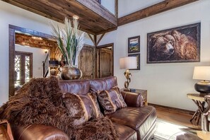 A cozy living room with a leather sofa, a decorative vase, and a bear painting on the wall. - Gorgeous 4BR Luxury Lodge! +Fire Pit +Large Yard (Sevierville)