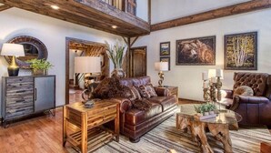 A spacious living room with a high ceiling, a large brown leather sofa, a wooden coffee table, and a rustic wooden staircase.
