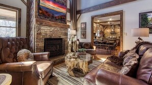 A spacious living room with a stone fireplace, leather sofas, and a dining area with a kitchen in the background.