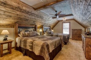 Une chambre avec deux lits, des poutres apparentes en bois au plafond, un ventilateur de plafond et une fenêtre avec des stores.
