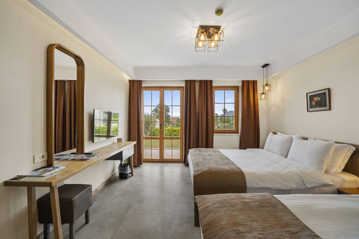 A hotel room with a bed, a desk, a mirror, and a large window with curtains.
