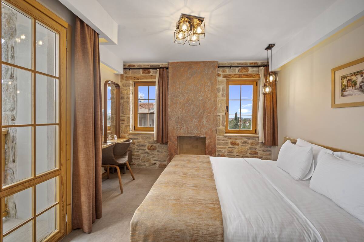 A bedroom with a large bed, a desk, and a fireplace.