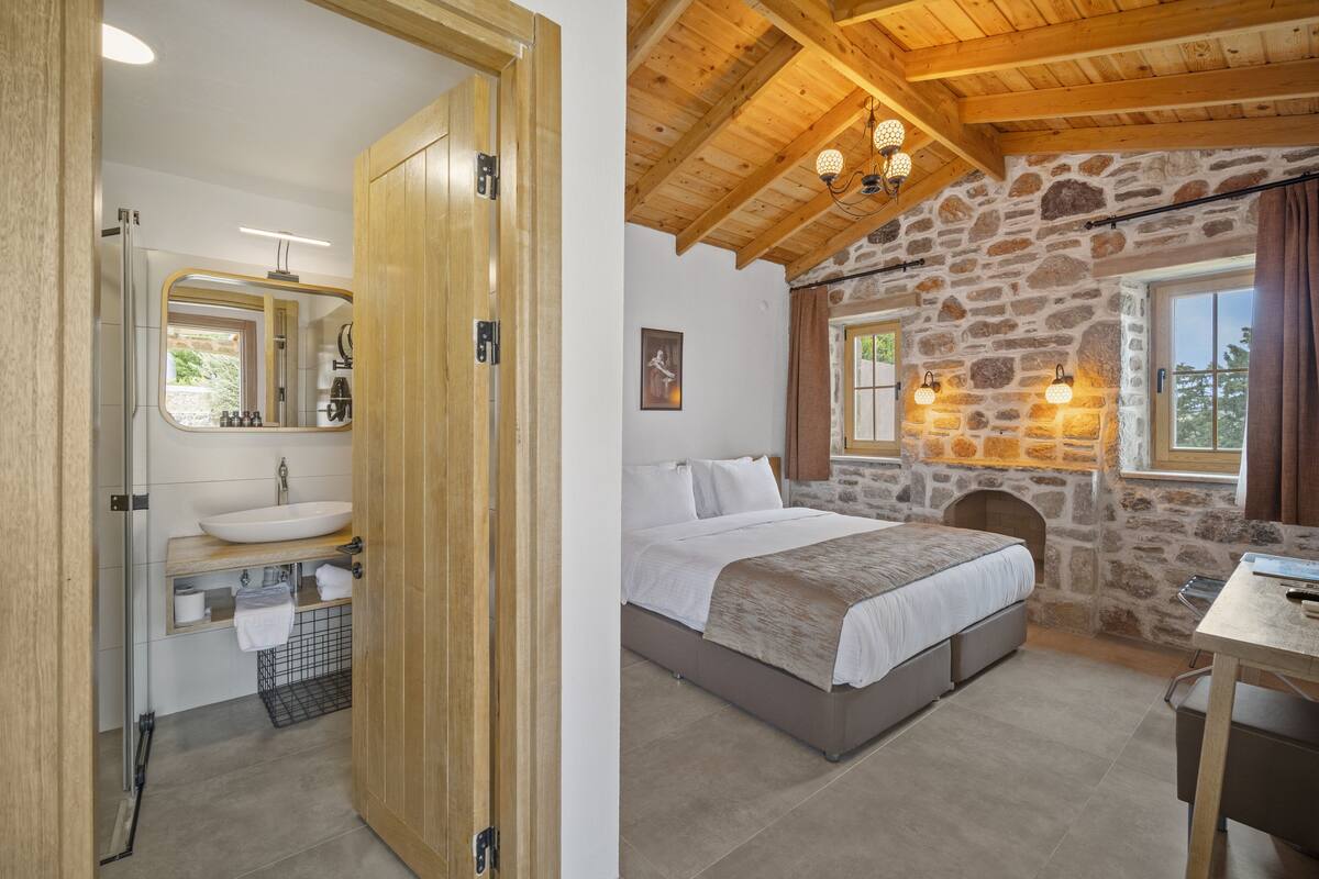A bedroom with a stone wall, a wooden ceiling, and a bed with a headboard.