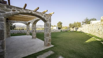 Una pérgola de piedra con techo de madera, un muro de piedra y un césped bien cuidado.