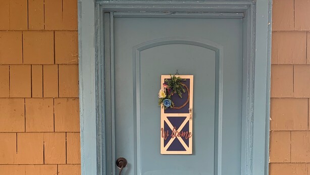 Una puerta azul claro con un cartel de bienvenida y un adorno de guirnalda.