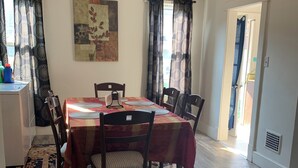 Un comedor con una mesa preparada para cuatro personas, rodeada de sillas, un tapete estampado y un ventilador de techo.