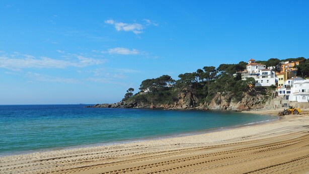 A beach with a clear blue sky, a sandy shore, and buildings on a cliff. - Modern apartment in Llafranc with A/C. No view (Llafranc)