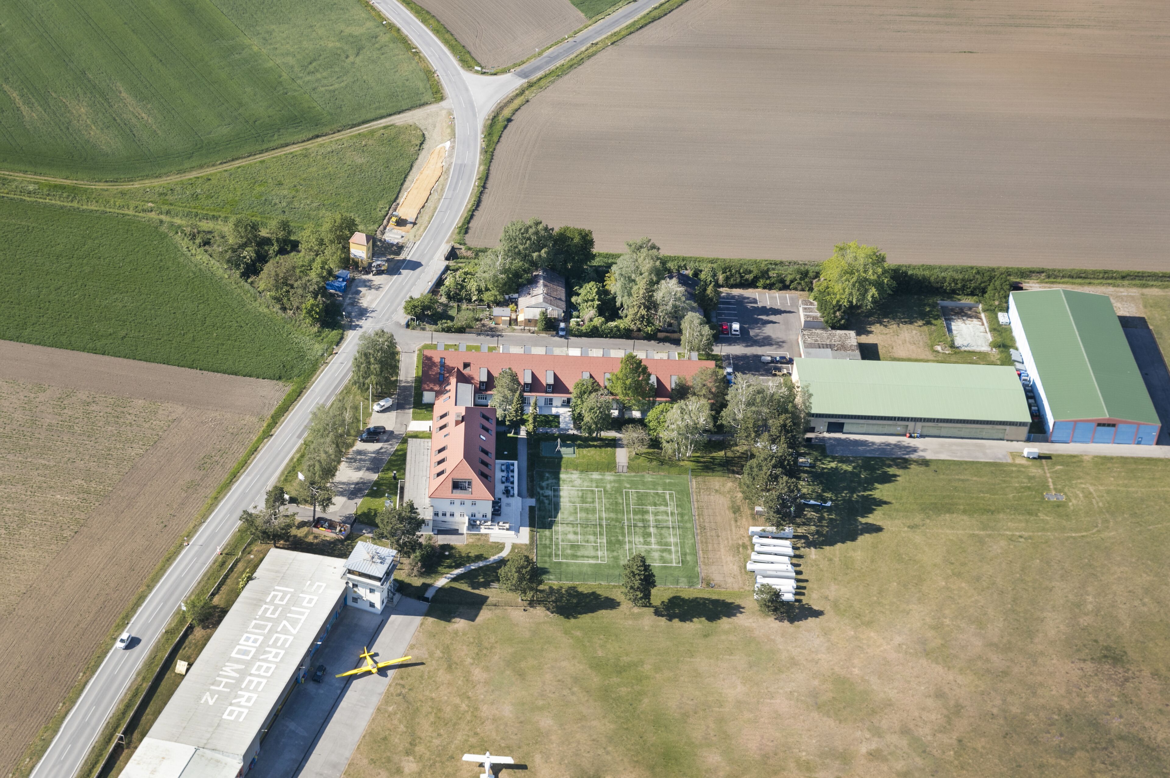 An aerial view of a property with a large building, sports field, and surrounding green fields.