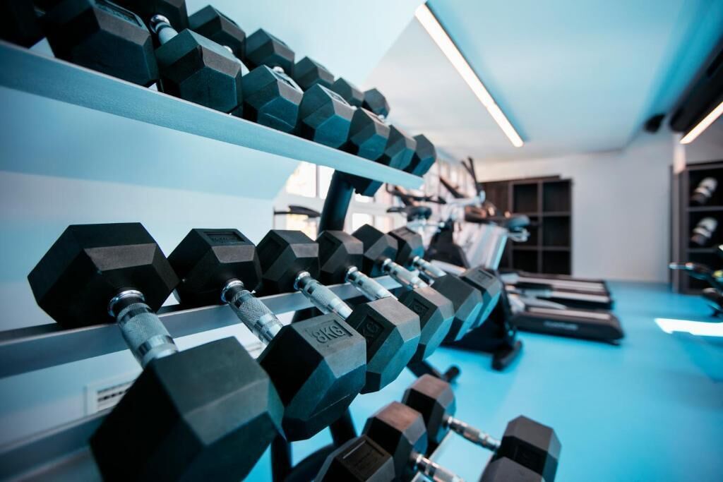 A gym with rows of hexagonal dumbbells on racks, a treadmill, and a blue floor.
