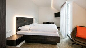 Un dormitorio moderno con cama, mesitas de noche, televisor y ventana con cortinas.