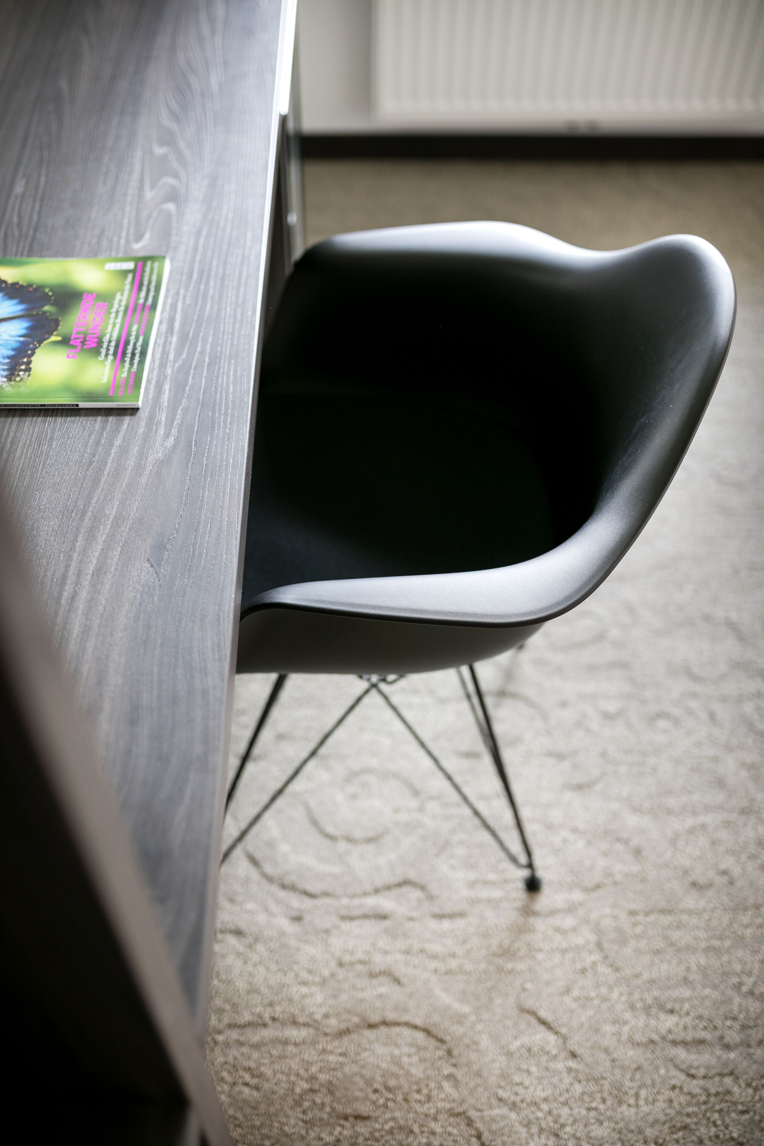 Une chaise moderne dotée d’un dossier incurvé et de pieds en métal, placée à côté d’une table en bois ornée d’une étiquette verte et rose.
