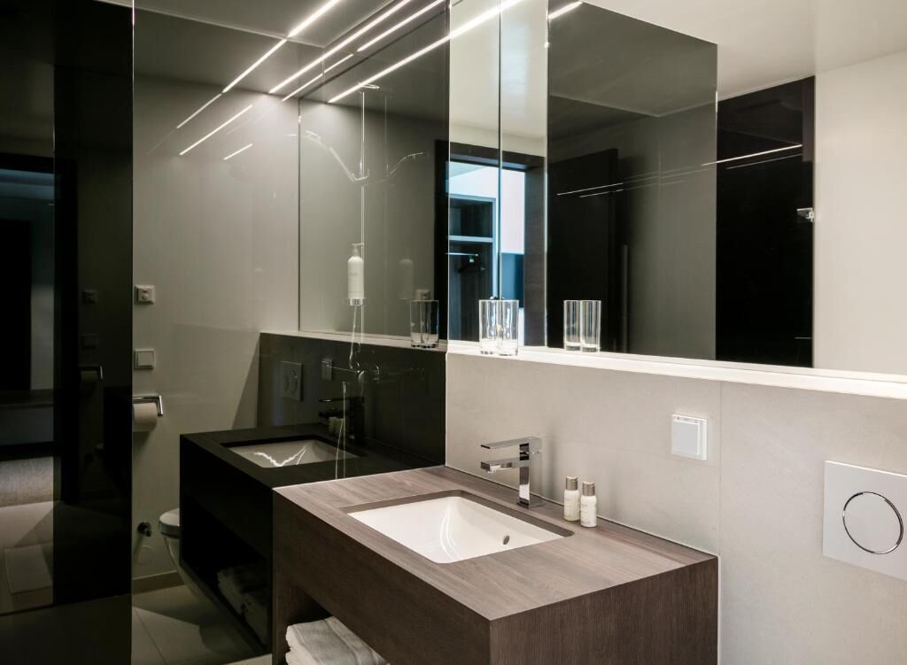 Un baño moderno con un espejo grande, dos lavamanos y una cabina de ducha de vidrio.