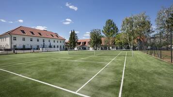 Un court de tennis avec un filet, entouré d’arbres et bordé d’un bâtiment dont le toit est rouge.