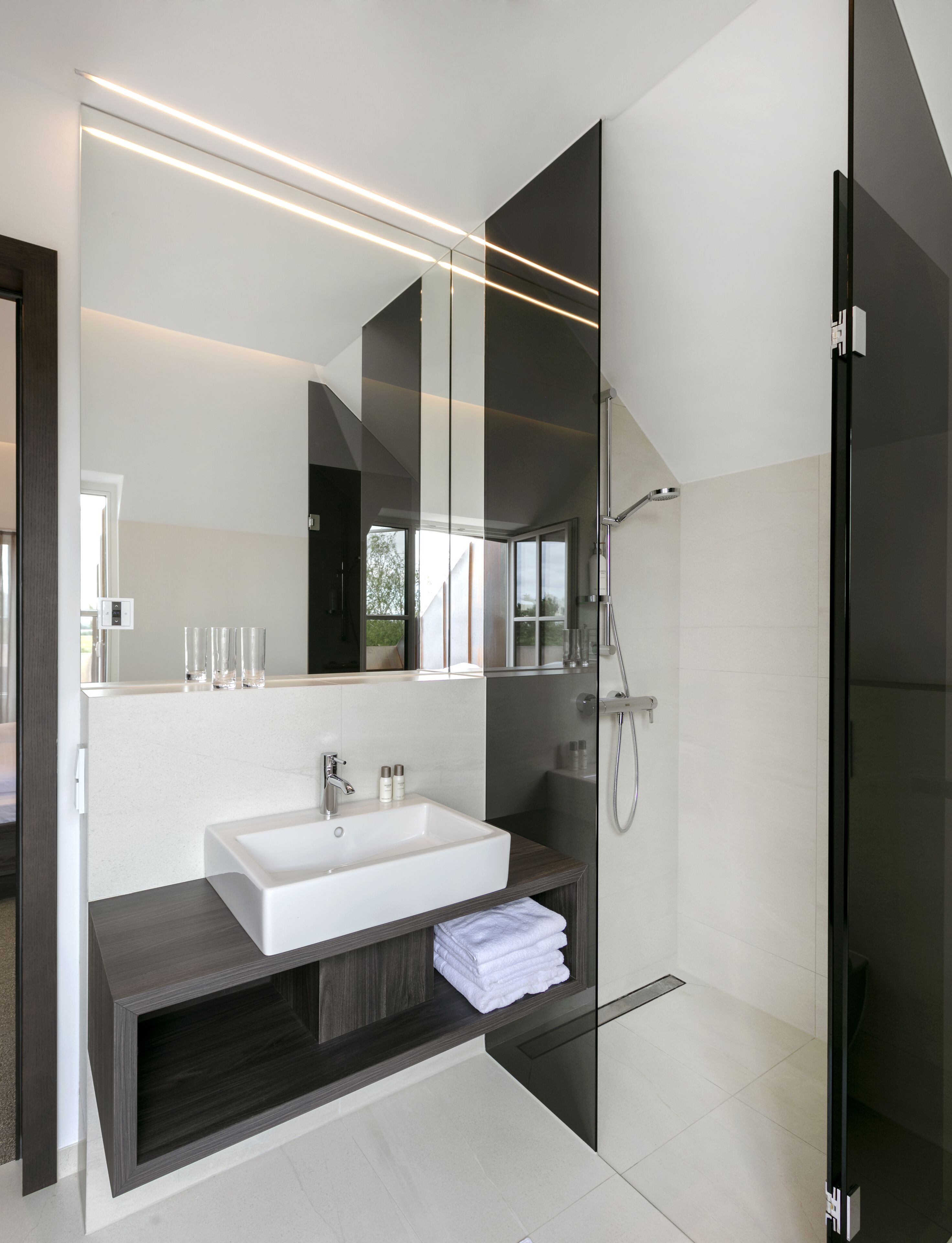 A modern bathroom with a large mirror, a white sink, a dark vanity, and a glass shower enclosure.