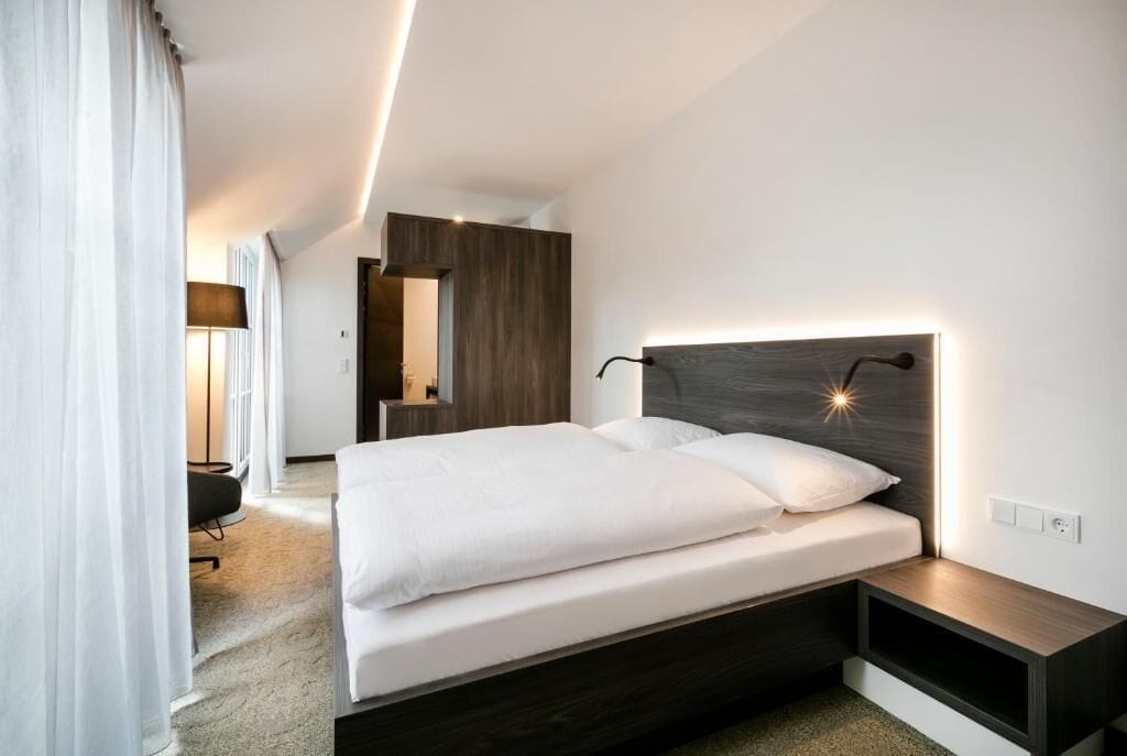 A modern hotel room with a large bed, a bedside table, and a built-in wardrobe.