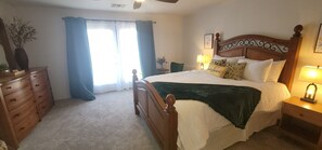 Une chambre à coucher avec un lit, des tables de chevet en bois, une commode, une fenêtre avec des rideaux et une lampe.