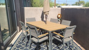 A balcony with a wooden table and chairs, a sunshade, and a decorative sunflower. - New house with fresh design available in Olsen TH. (Tucson)