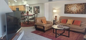 Un salon comprenant un téléviseur, un canapé, un fauteuil, une table basse et un coin repas avec une table et des chaises.