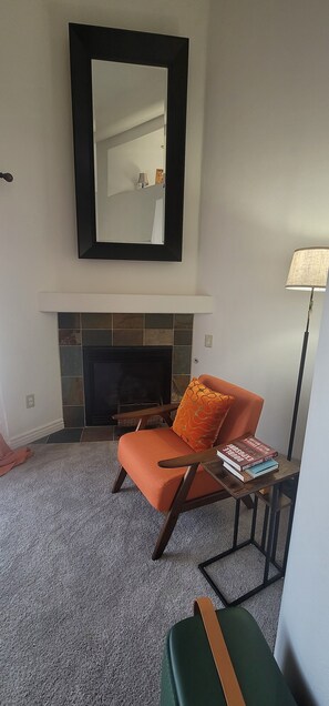 Un salon avec une cheminée, un canapé, une table avec des livres et un lampadaire.