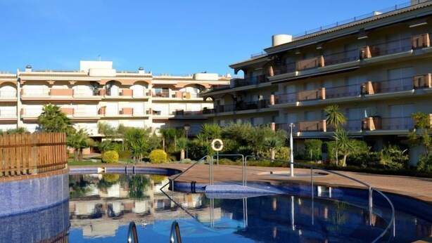 Una piscina con bordo piastrellato, circondata da un percorso pedonale in mattoni, adiacente a un edificio a più piani con balconi.