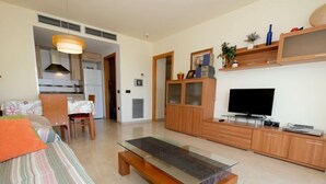Un soggiorno moderno con un divano, un tavolino in vetro, una televisione e mobili contenitori in legno.