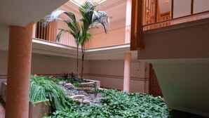 Atrio a più livelli con una fontana centrale, circondato da vegetazione rigogliosa e una palma.