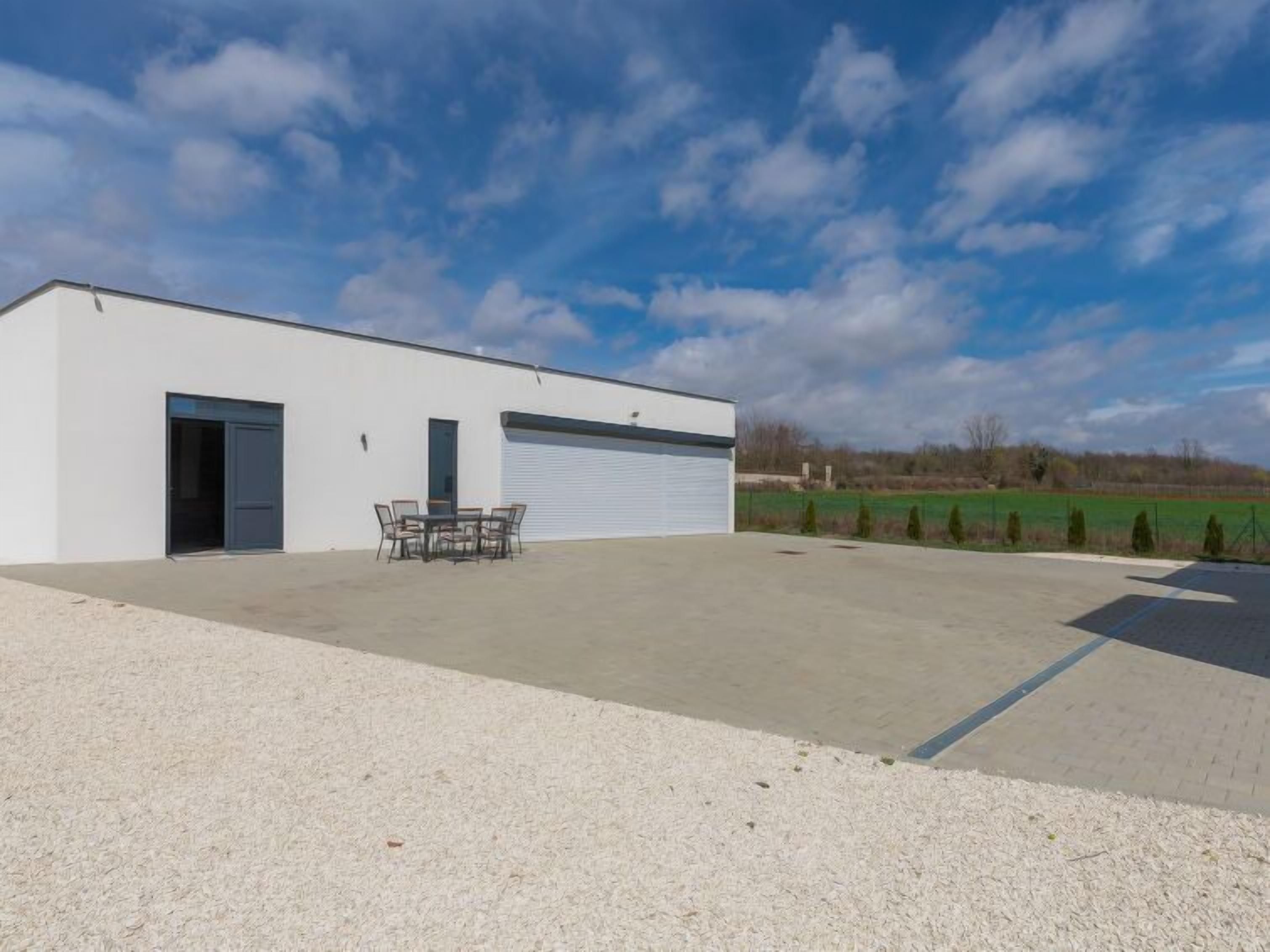 Un bâtiment moderne doté d’une porte de garage, d’un patio avec mobilier d’extérieur et d’une allée gravillonnée.