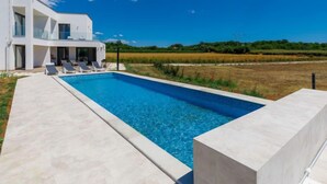 Una casa moderna a due piani con piscina, sedie a sdraio e vista su un campo.