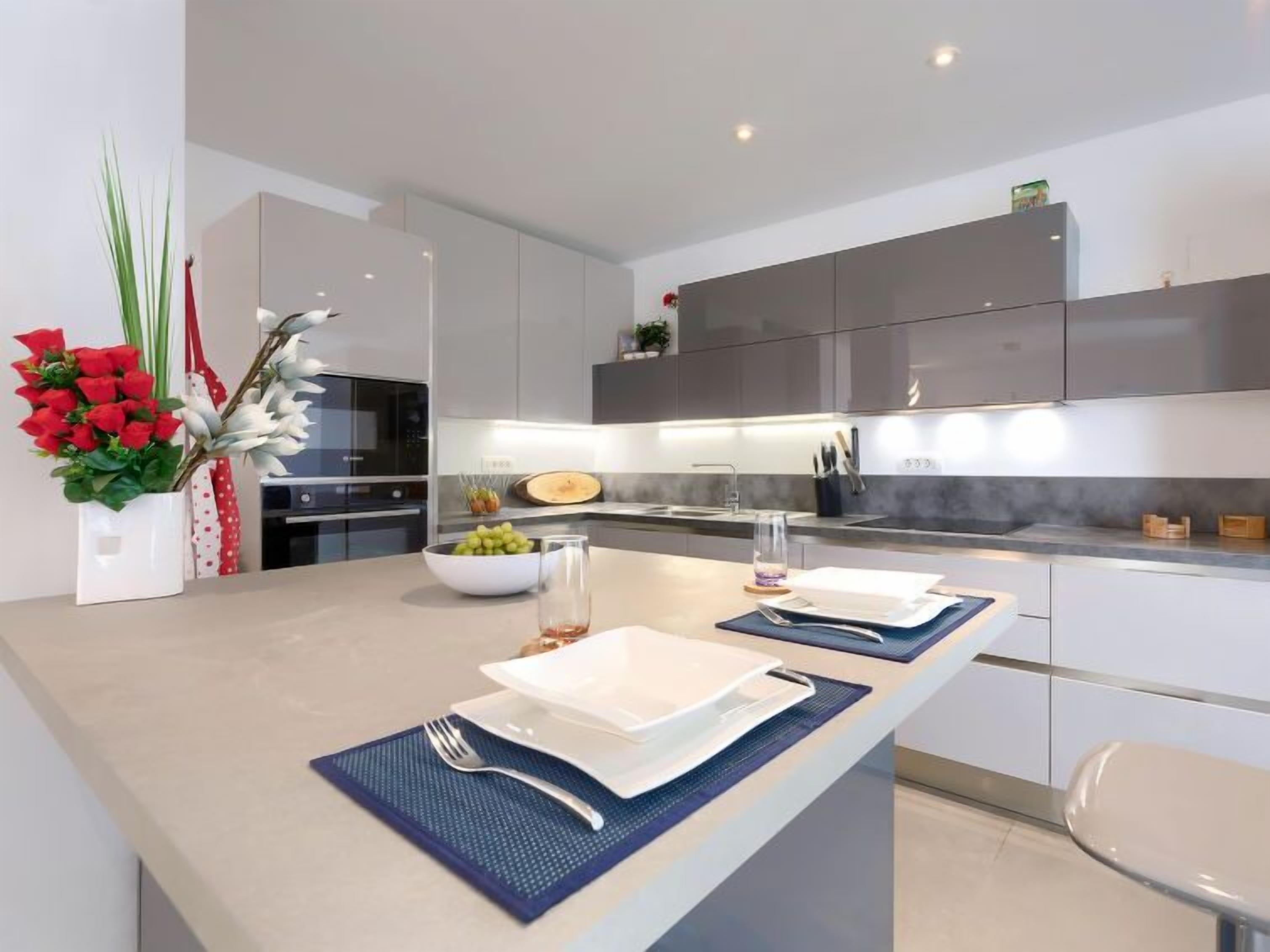 Una cocina moderna con una isla central, armarios blancos y una campana extractora de acero inoxidable.