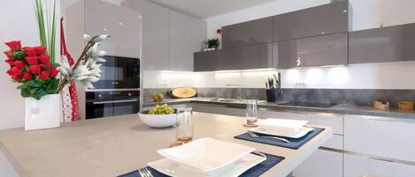 Una cocina moderna con una isla central, armarios blancos y una campana extractora de acero inoxidable.