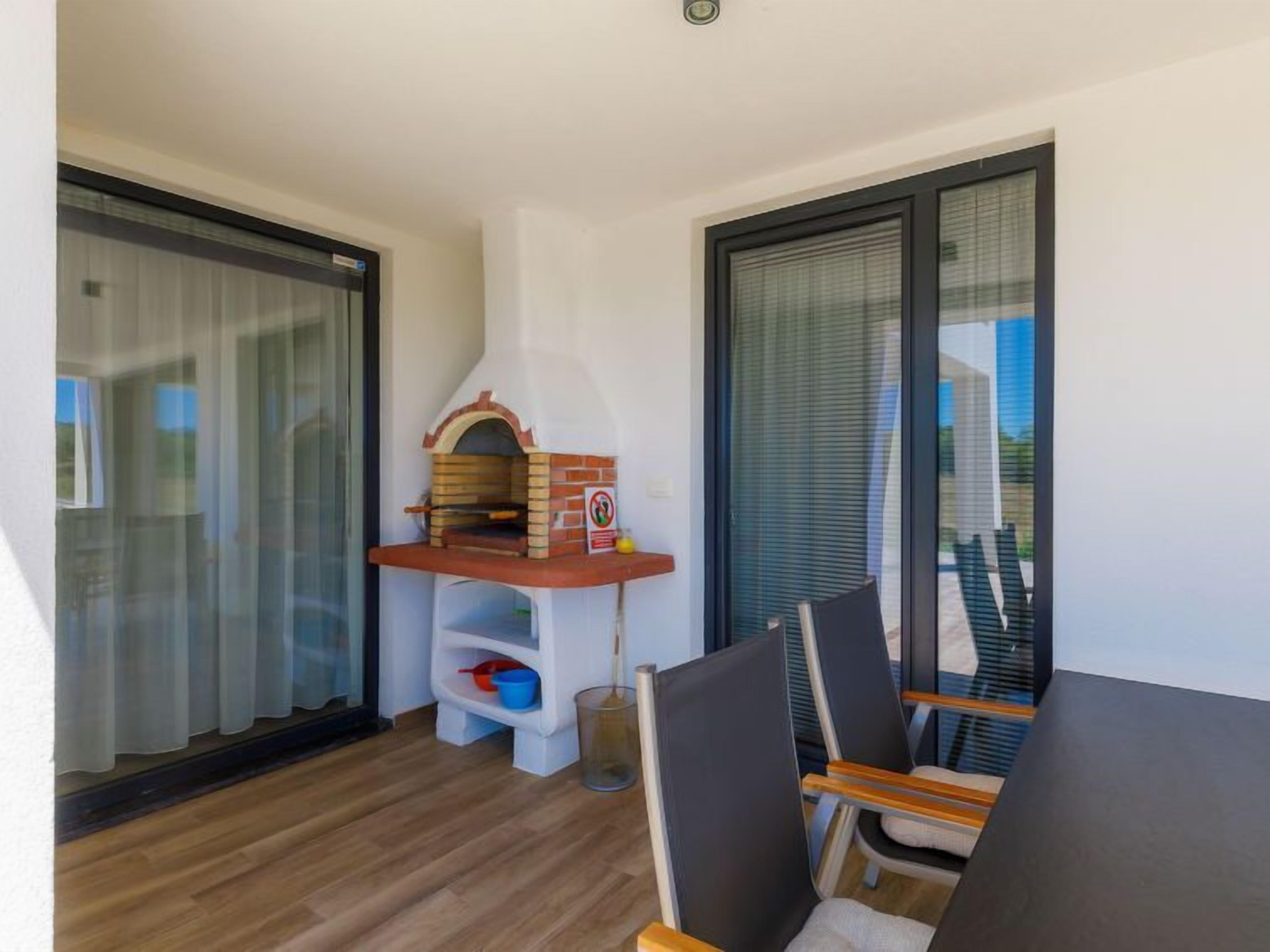 A balcony with a small brick oven, a table with chairs, and a window with blinds.