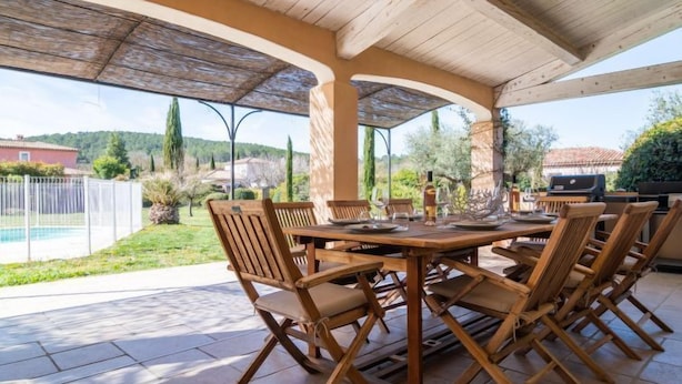 Un patio al aire libre con una mesa y sillas de madera, una parrilla y vistas del paisaje circundante.