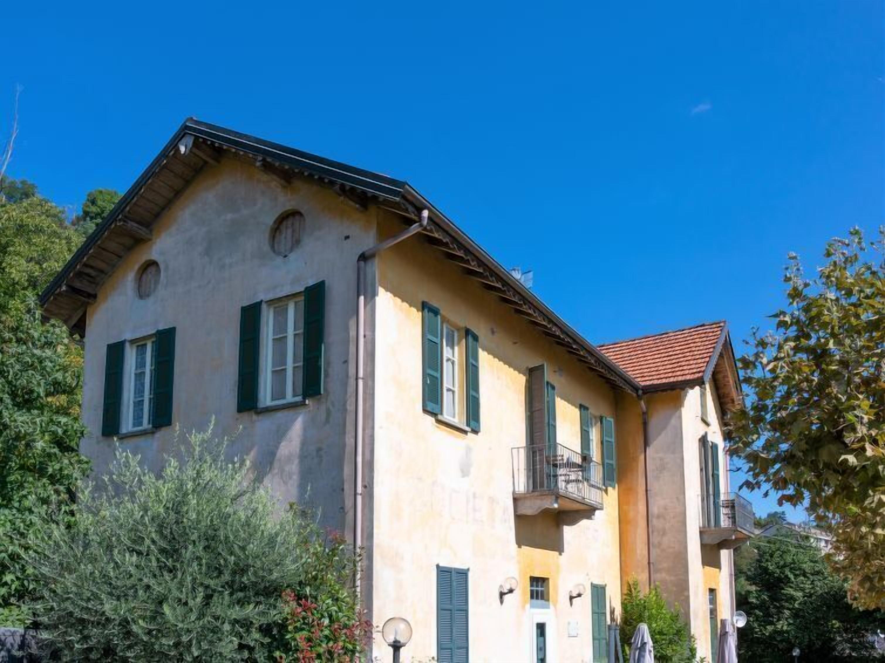 A two-story building with a sloped roof, green shutters, and a balcony on the second floor.