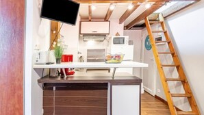 Una cucina compatta con TV integrata, mobili bianchi e soffitto in legno.