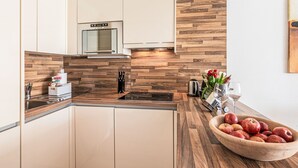 A modern kitchen with wooden accents, a built-in microwave, and a bowl of apples on the counter. - Apartment Emma by Interhome (Kaprun)