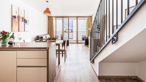 A modern kitchen with a dining area, wooden flooring, and a staircase with black railings. - Apartment Emma by Interhome (Kaprun)