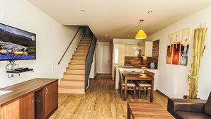 A modern living space with a wooden staircase, a dining area, a kitchen, and a flat-screen TV mounted on the wall. - Apartment Emma by Interhome (Kaprun)