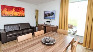Un salon moderne avec un canapé en cuir foncé, une table à manger en bois agrémentée d’un vase décoratif, un téléviseur à écran plat et un tableau accroché au mur.