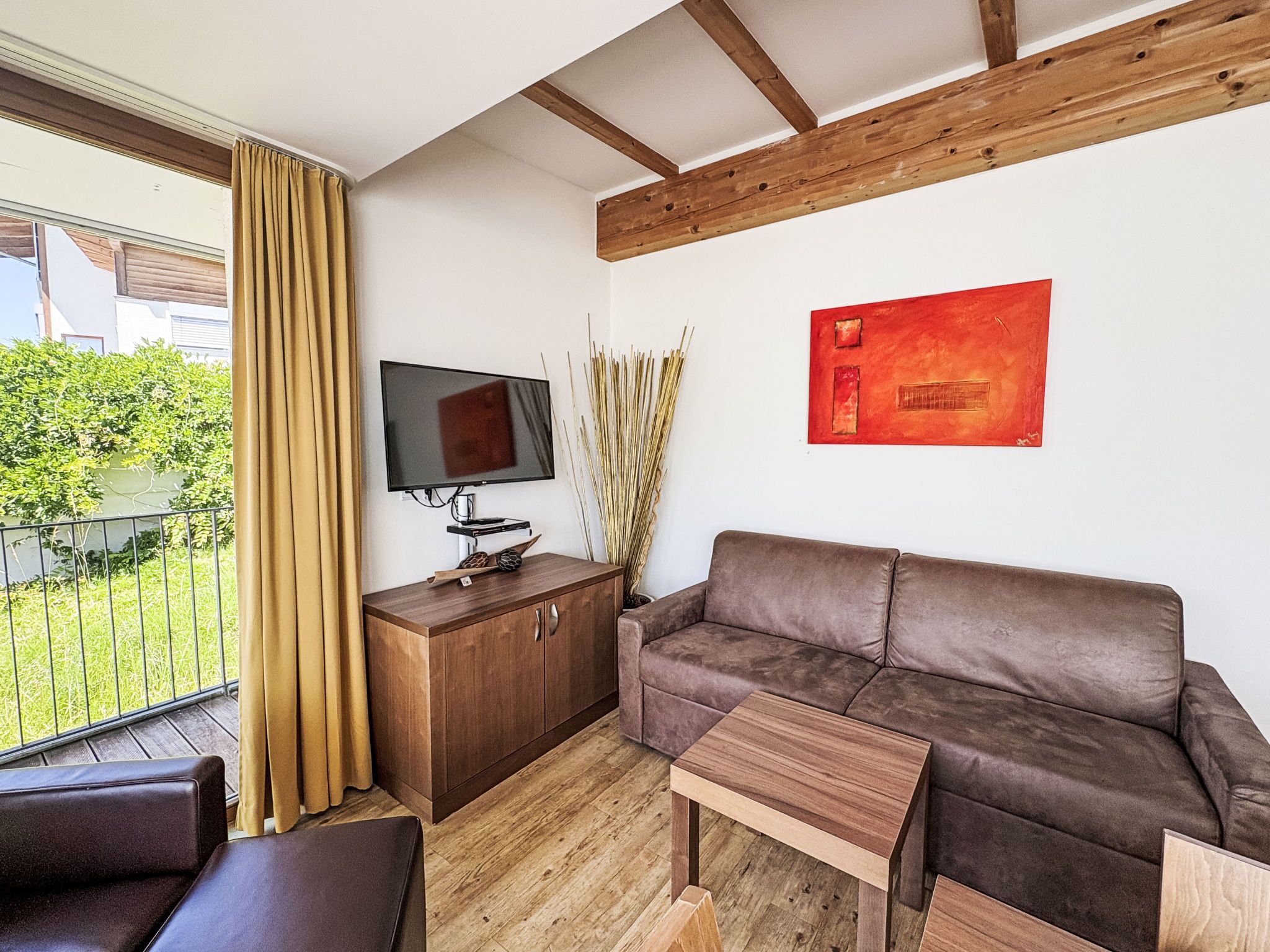 Un salon moderne avec un plafond en bois, un canapé en cuir marron, une table basse en bois, un téléviseur posé sur un meuble en bois et un tableau abstrait rouge accroché au mur.