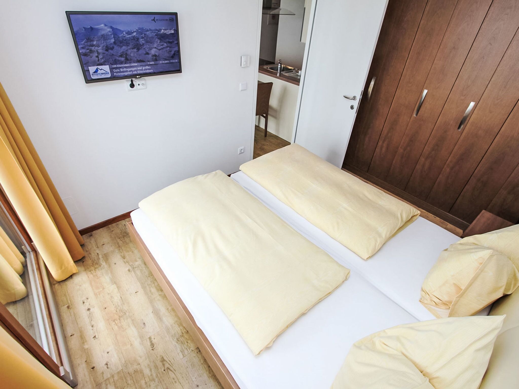 Een hotelkamer met twee bedden, een aan de muur bevestigde televisie en een houten garderobe.
