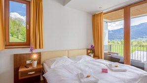 A hotel room with a large bed, wooden nightstand, and a window with curtains. - Apartment Emma by Interhome (Kaprun)