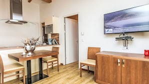 A modern kitchen with a dining area, wooden flooring, a TV mounted on the wall, and a red kettle on the counter. - Apartment Emma by Interhome (Kaprun)